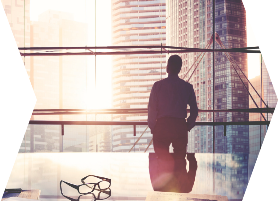 A business man in his office looking out of the window at high-rise buildings.