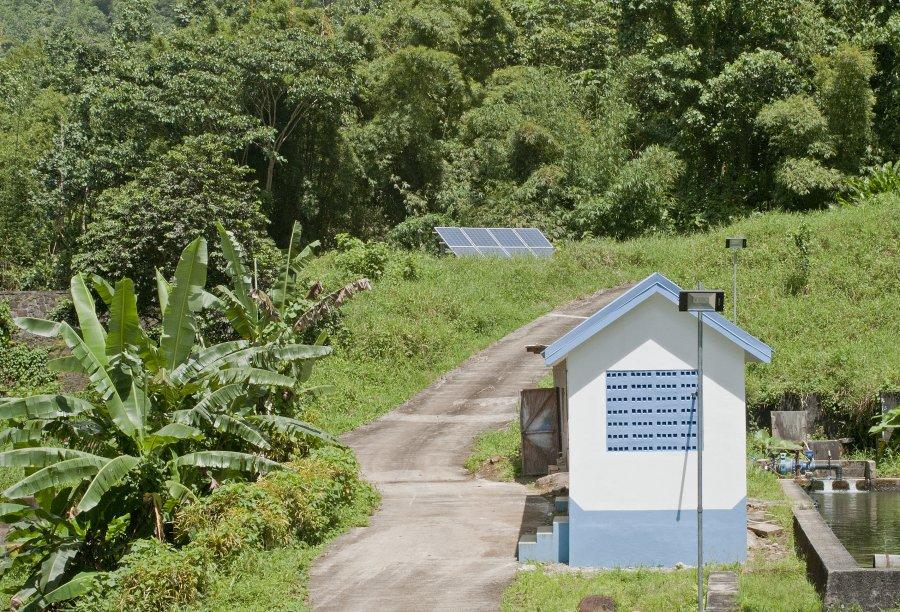 A solar panel within a green landscape and next to a small cottage.