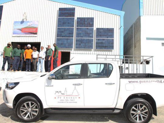 The PV Energy Team with a branded car and a warehouse banner.