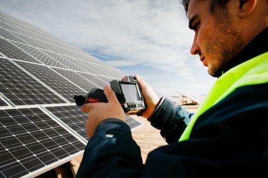 Engineer with camera next to a solar panel.