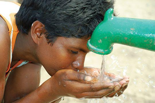 Young boy drinking water from tap.